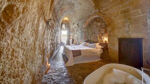 Habitación de paredes de piedra con cama, bañera y una pequeña mesa con silla.