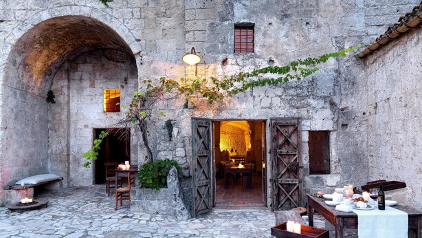 Un patio al aire libre con suelo de piedra, muebles de madera rústica y una mesa lista para comer.