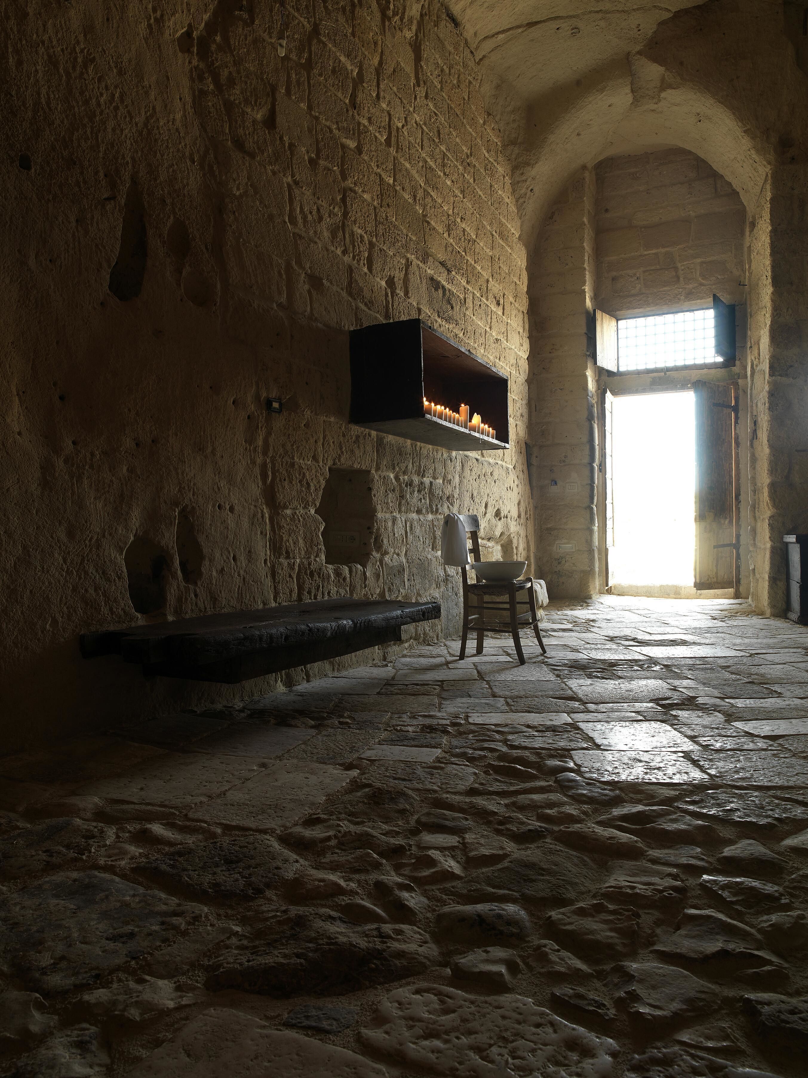 A stone-walled room with a bench, a table, and a window with a view.