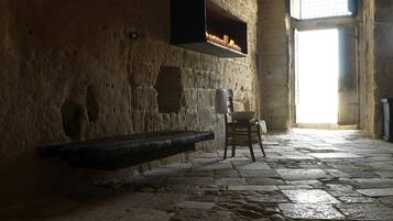 A stone-walled room with a bench, a table, and a window with a view.