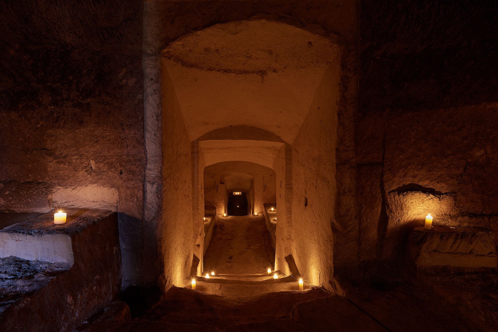 An underground passageway with stone walls and a series of candles providing light.