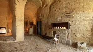 Una habitación con paredes de piedra, una cama, un banco de piedra y un estante con velas.