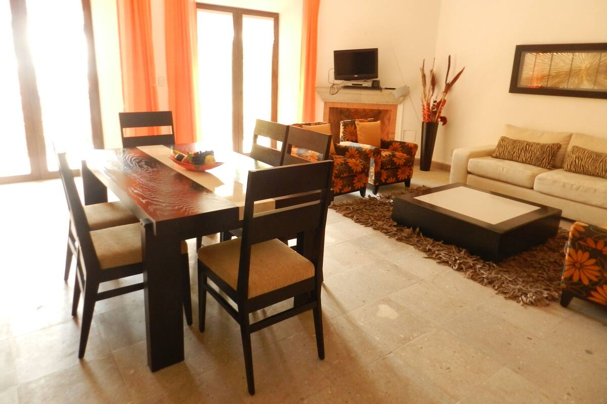 Un comedor con una mesa y sillas de madera, un sofá y un televisor sobre un mueble.