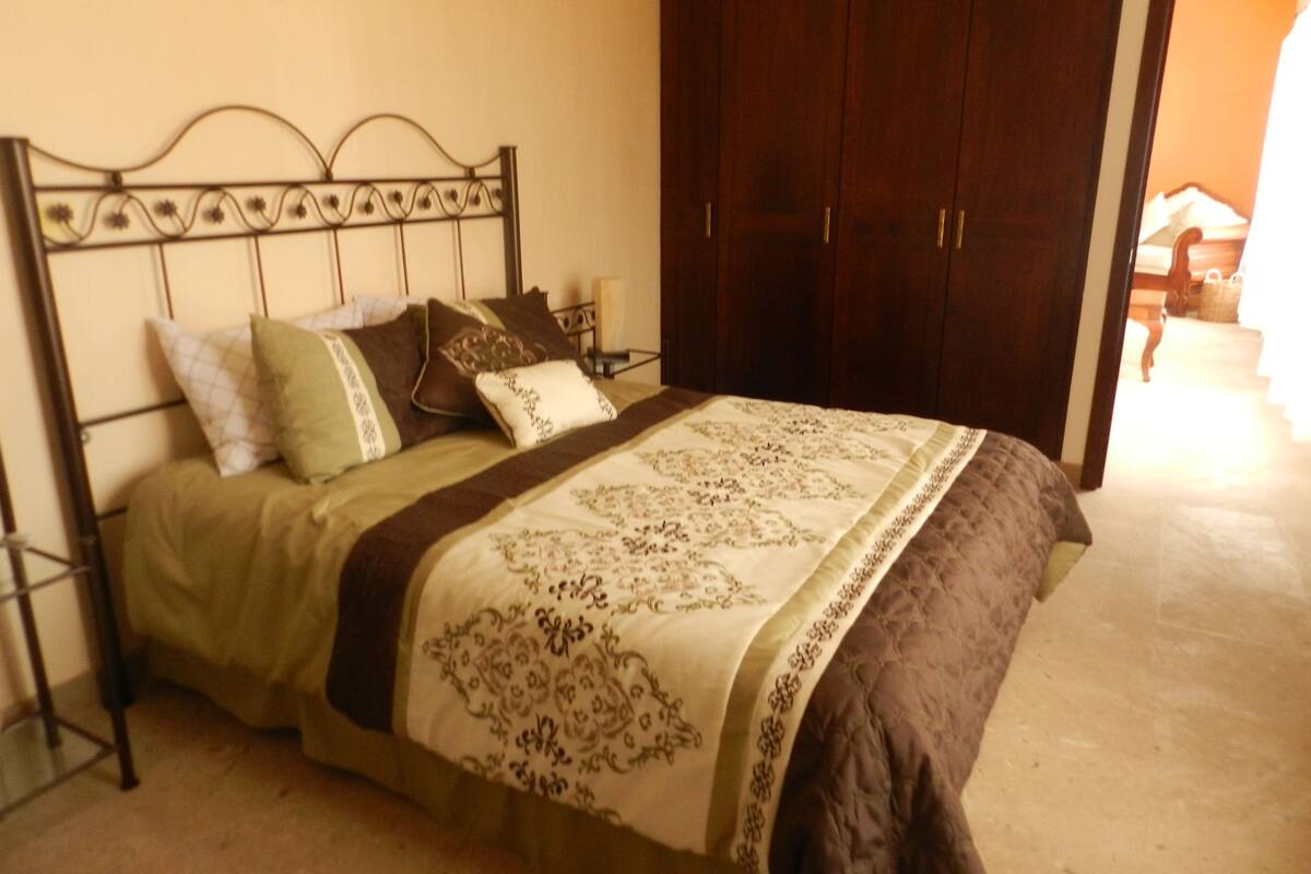 Una cama con cabecera de metal, colcha marrón y varias almohadas.