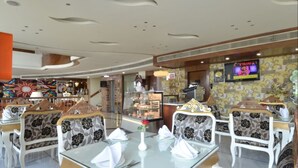 En restaurant med hvide stole med blomstermønster, glasborde og et fjernsyn på væggen.