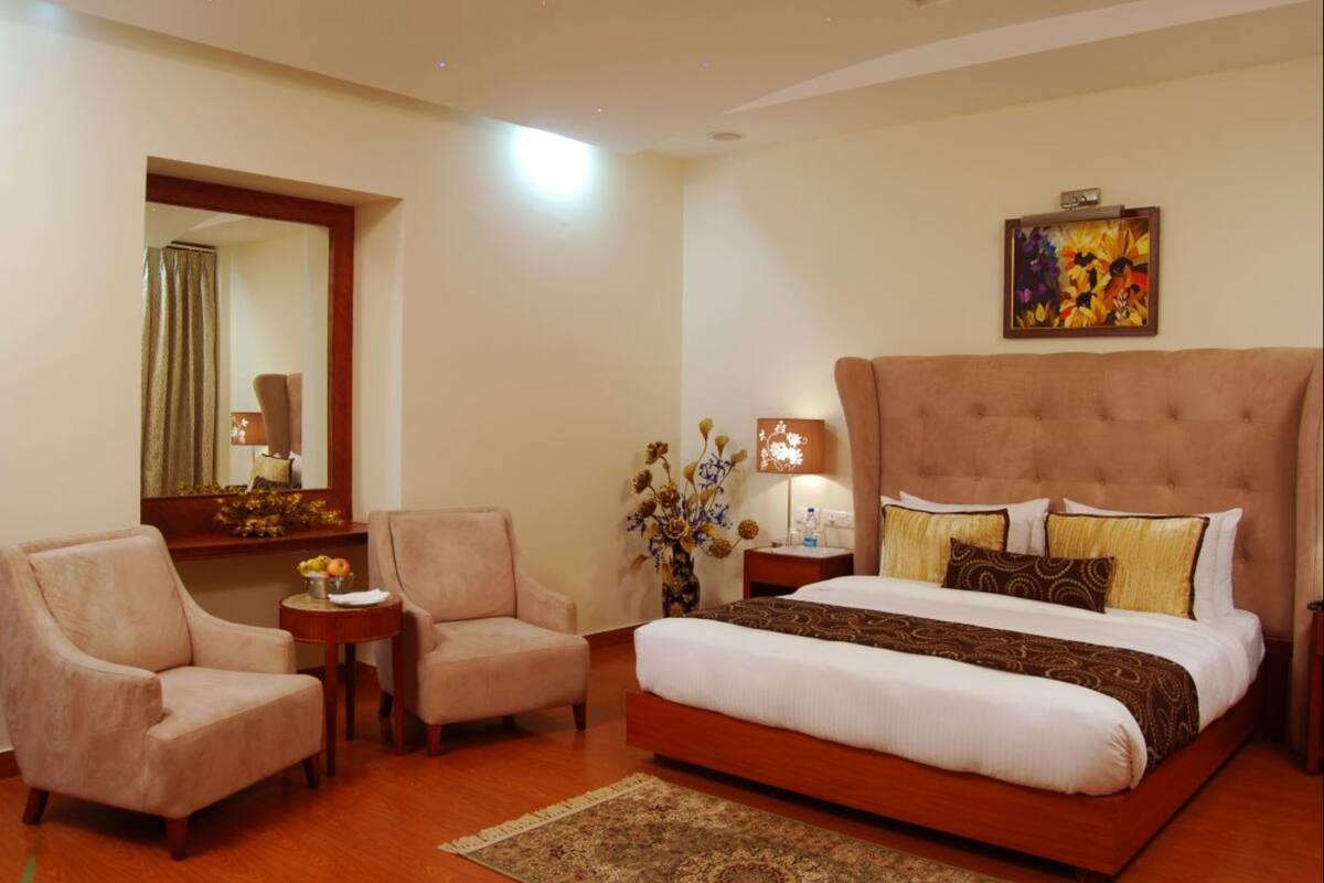 A hotel room with a large bed, two armchairs, a small table, a mirror, a vase with flowers, and a painting on the wall.
