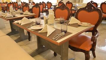 Un comedor con mesas dispuestas para el servicio, sillas con respaldos decorados y un suelo pulido.