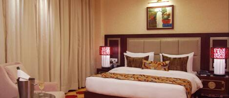 A hotel room with a large bed, a sitting area with a chair and a small table, and a ceiling fan.