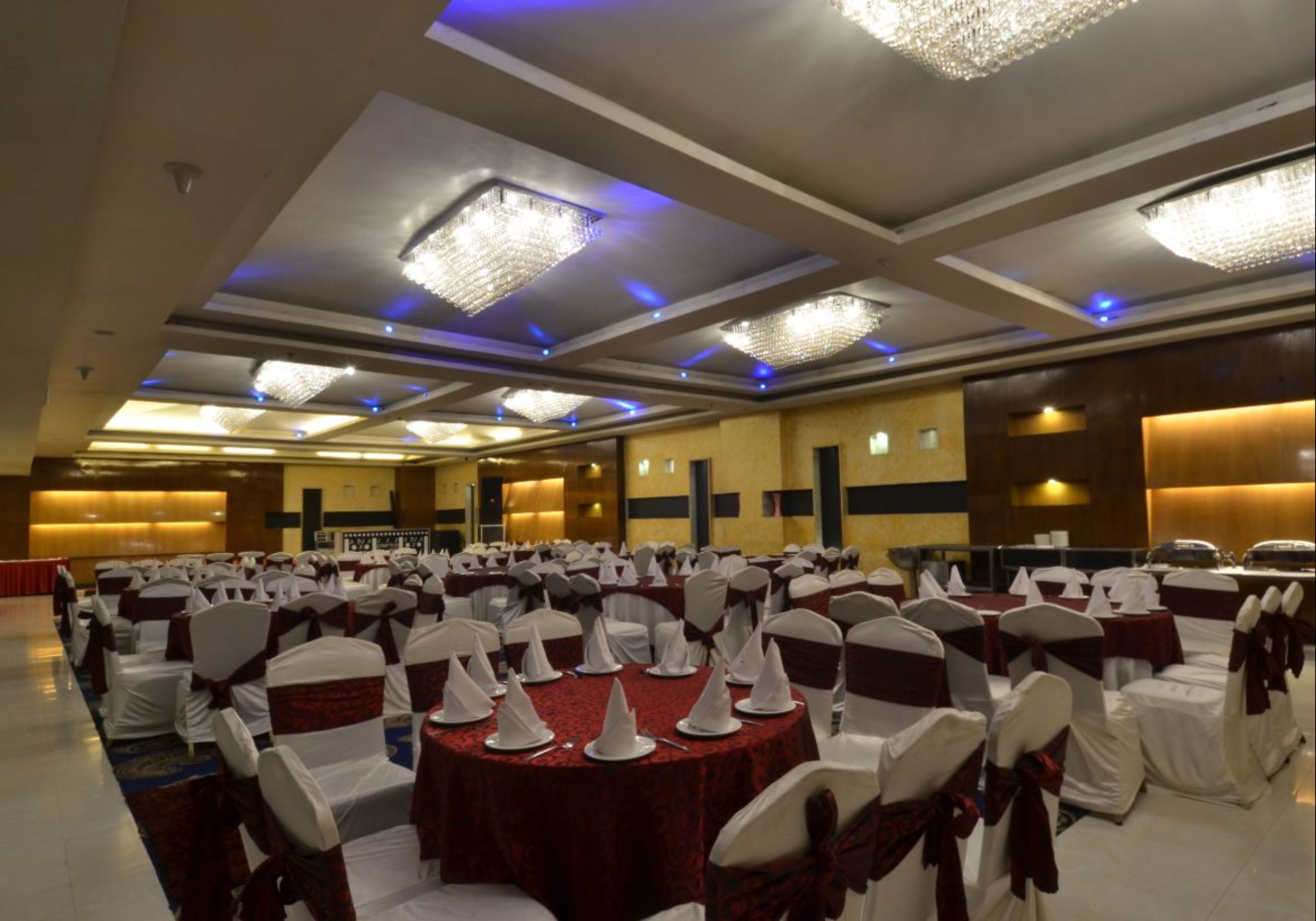 A banquet hall with round tables, white chairs with red sashes, and chandeliers.