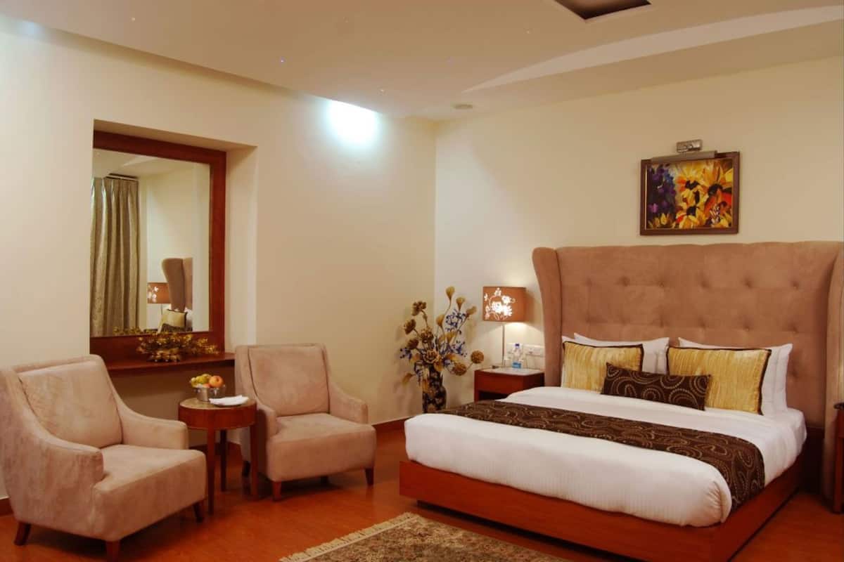 A hotel room with a large bed, two armchairs, a nightstand, a mirror, and a painting on the wall.