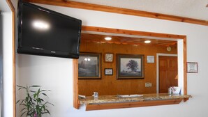 A reception area with a wooden counter, a television mounted above it, a clock, framed pictures, and a sign for Cherokee Casino Shuttle Service. - Budget Inn Siloam Springs (Siloam Springs)