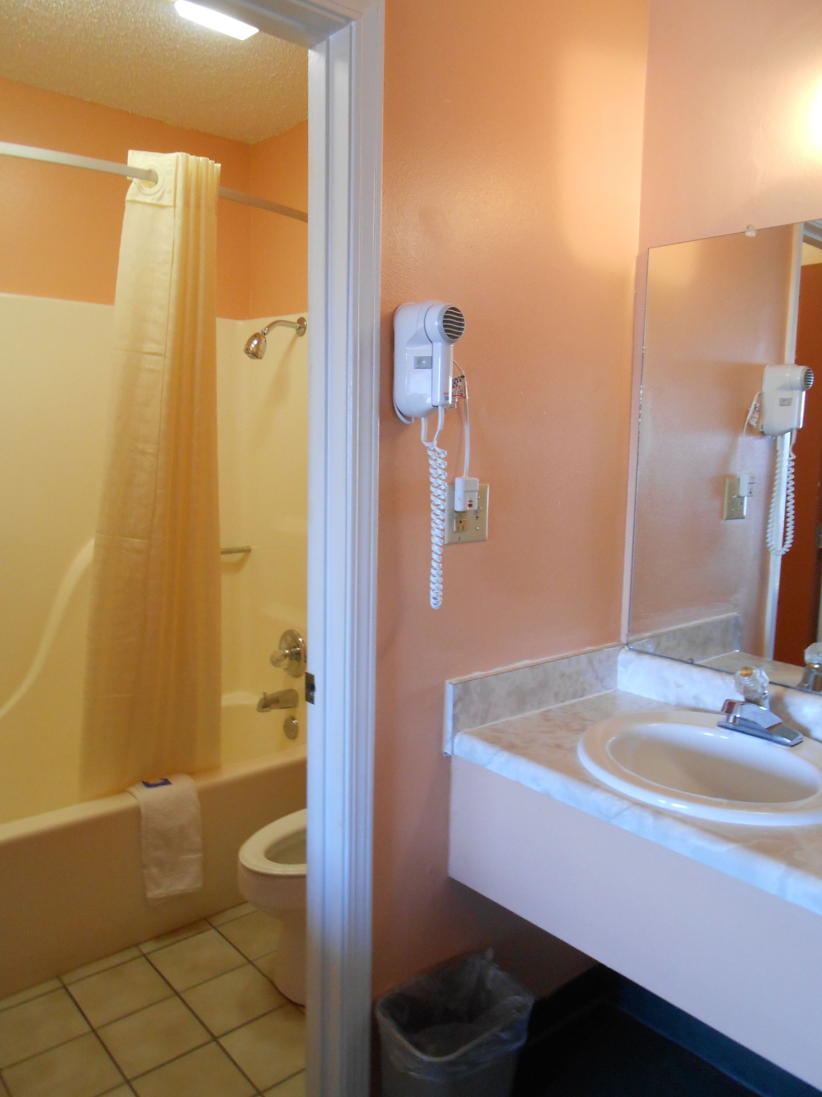 A bathroom with a bathtub, toilet, and sink. There is a hairdryer on the wall and a trash can next to the sink.