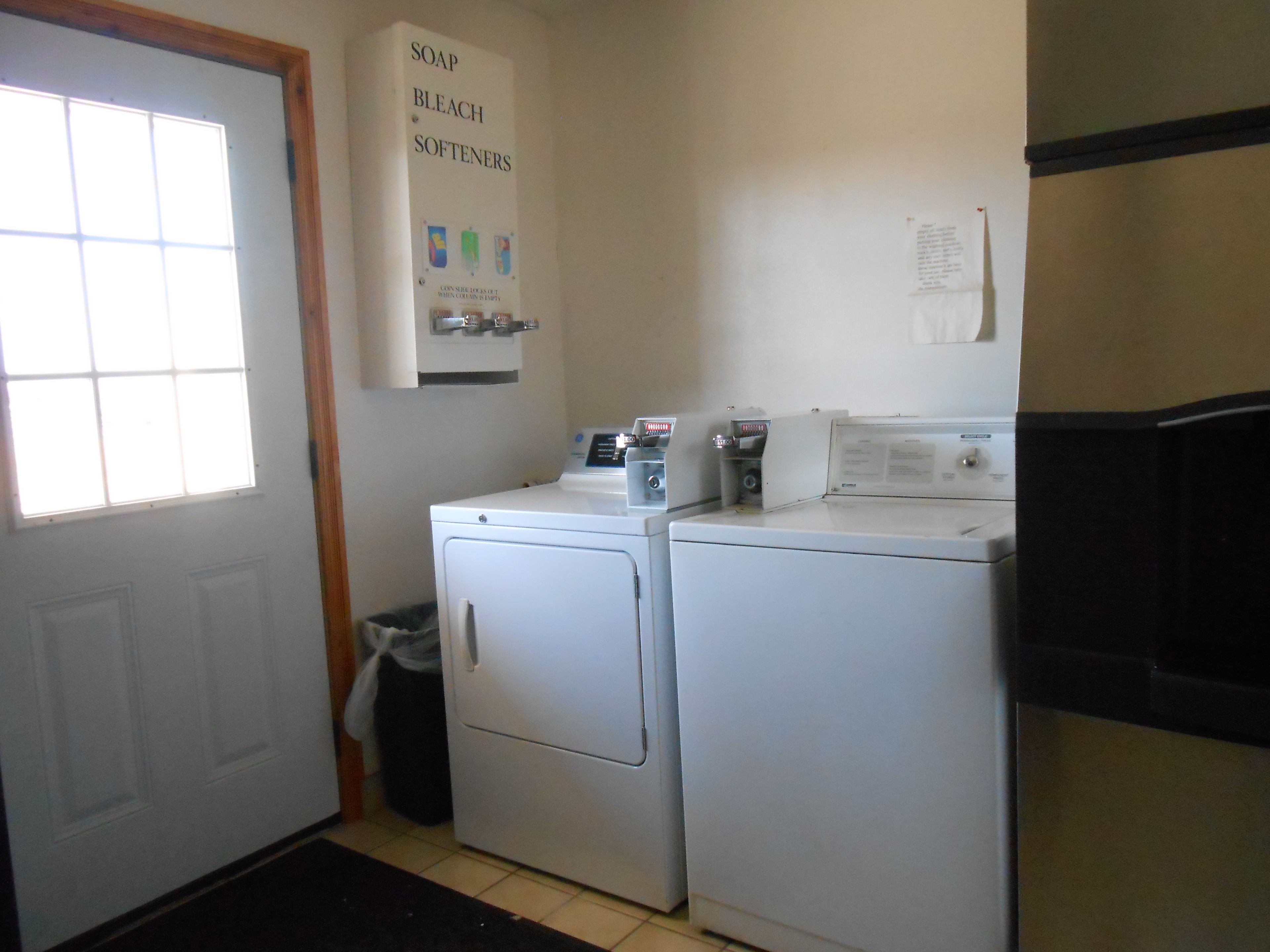 A laundry room with two front-loading washers and dryers, a window, and a sign above the washers.
