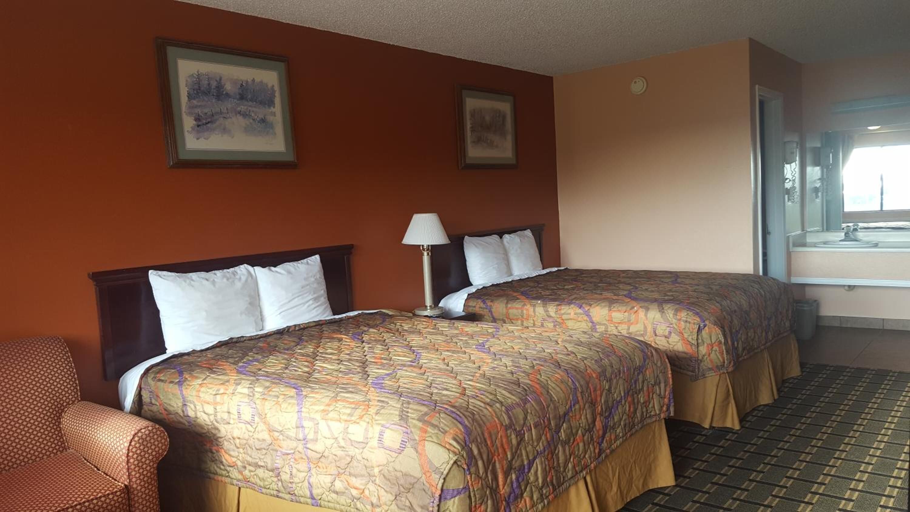 A hotel room with two beds, a chair, and a window with a view.