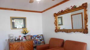 A living room with a wooden cabinet, a coffee maker, a magazine rack, and a red patterned sofa. - Budget Inn Siloam Springs (Siloam Springs)