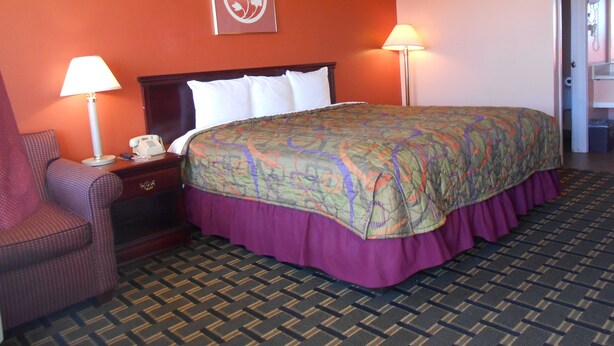 A hotel room with a large bed, two bedside lamps, a chair, and a wall clock. - Budget Inn Siloam Springs (Siloam Springs)