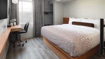 Una habitación de hotel con cama, escritorio, silla, armario y ventana con cortinas.
