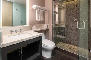 Un baño moderno con un lavabo blanco, un inodoro, una ducha con mampara de vidrio y un perchero con dos toallas.