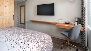 A hotel room with a bed, a desk with a chair, a television, and a coffee machine.