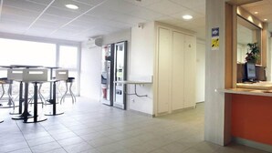 A reception area with a counter, a waiting area with tables and chairs, and a door leading to a room. - Sweet and Smart Hotel - formerly Premiere Classe Hambach (Hambach)