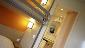 A compact hotel room with a bunk bed, a small bedside table, a wall-mounted TV, and a bathroom with a toilet and sink. - Sweet and Smart Hotel - formerly Premiere Classe Hambach (Hambach)