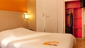 A hotel room with a bed, a desk with a computer, a wardrobe, and a closet with hanging clothes. - Sweet and Smart Hotel - formerly Premiere Classe Hambach (Hambach)