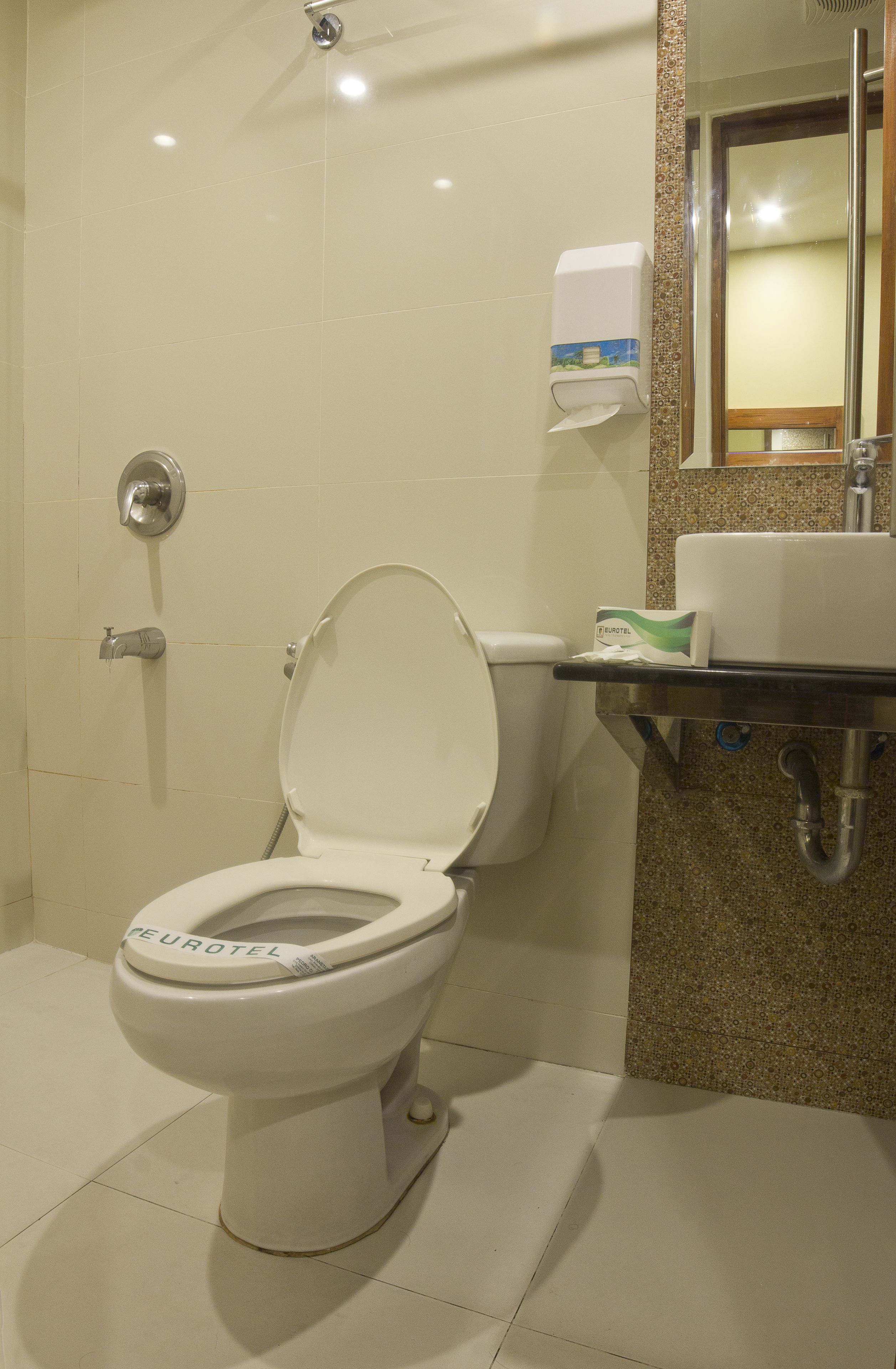 A modern bathroom with a white toilet, a hand dryer, and a sink with a mirror above it.