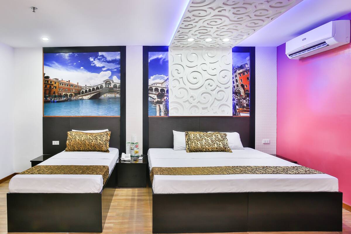 A hotel room with two beds, a large mural of a cityscape, a modern air conditioning unit, and a decorative ceiling panel.