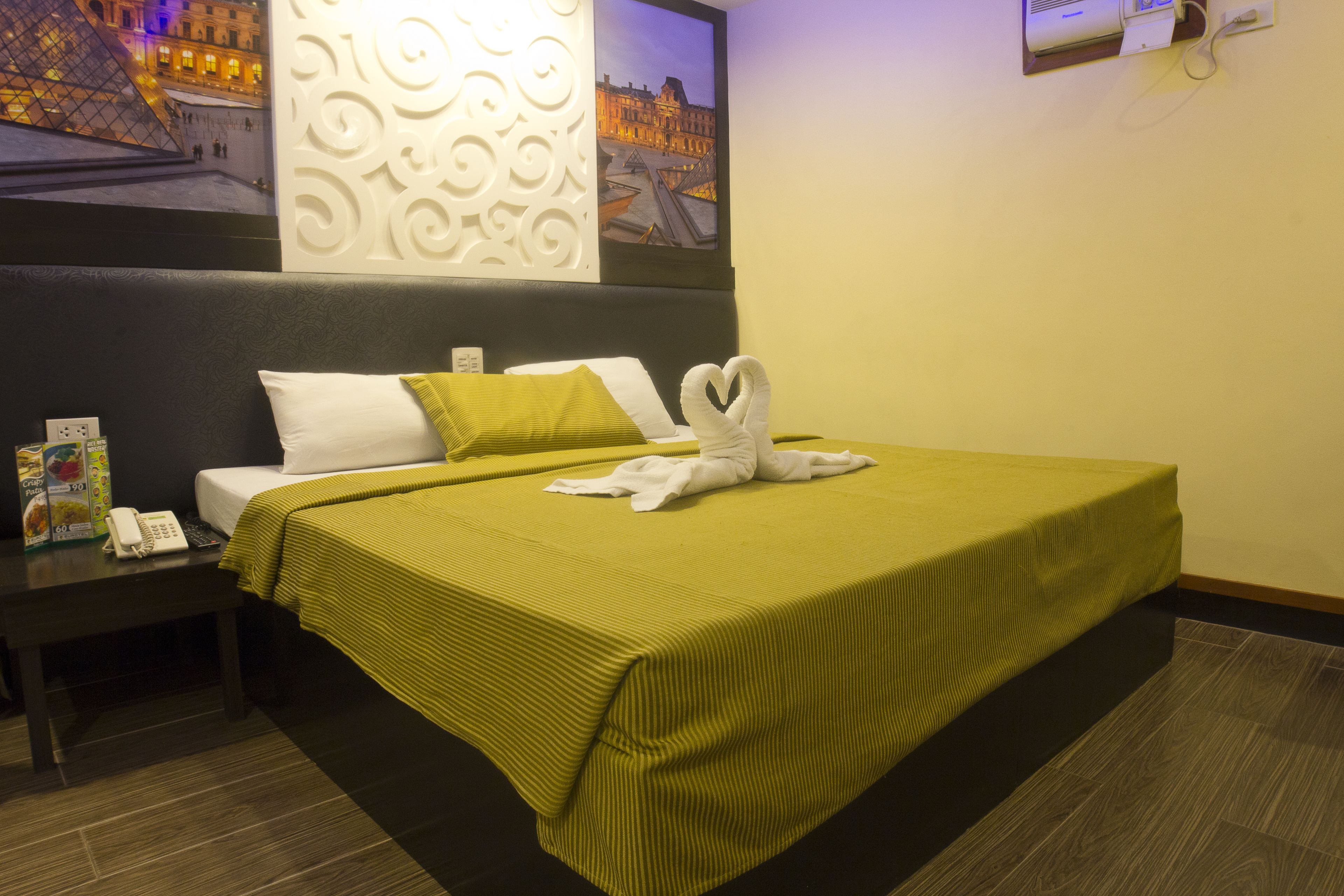 A hotel room with a bed, a nightstand, a telephone, and a wall decoration.