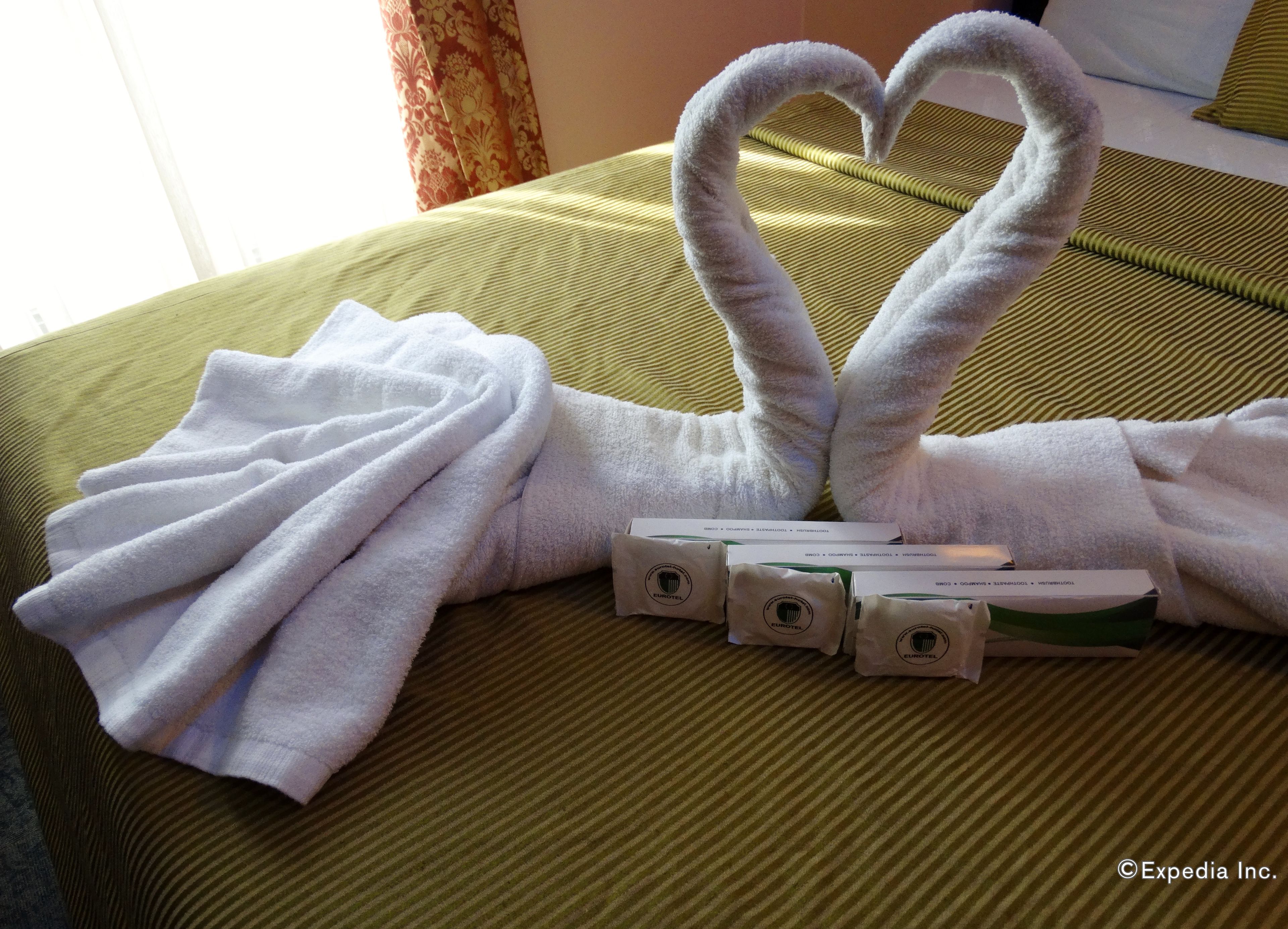 A neatly made bed with a heart-shaped towel arrangement and a set of toiletries.