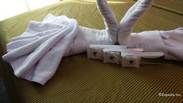A neatly made bed with a heart-shaped towel arrangement and a set of toiletries.