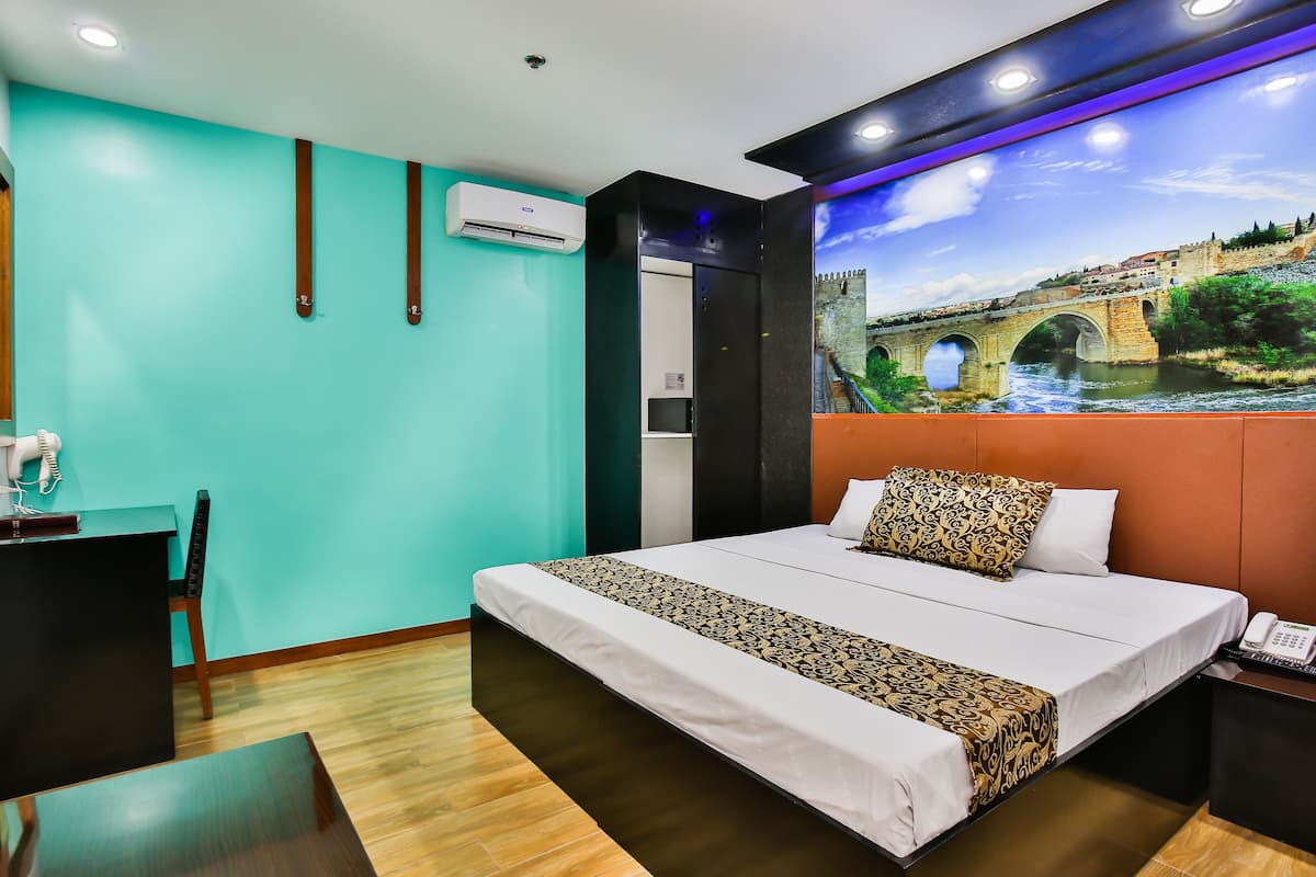 A hotel room with a bed, a desk, and a chair. There is a painting of a bridge on the wall.