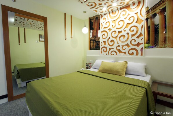 Quarto de hotel com cama, espelho, painel decorativo na parede e luminária suspensa.