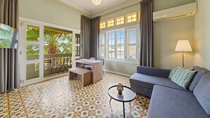 Ein Zimmer mit Balkon, einer Couch, einem Tisch und einem Fernseher.