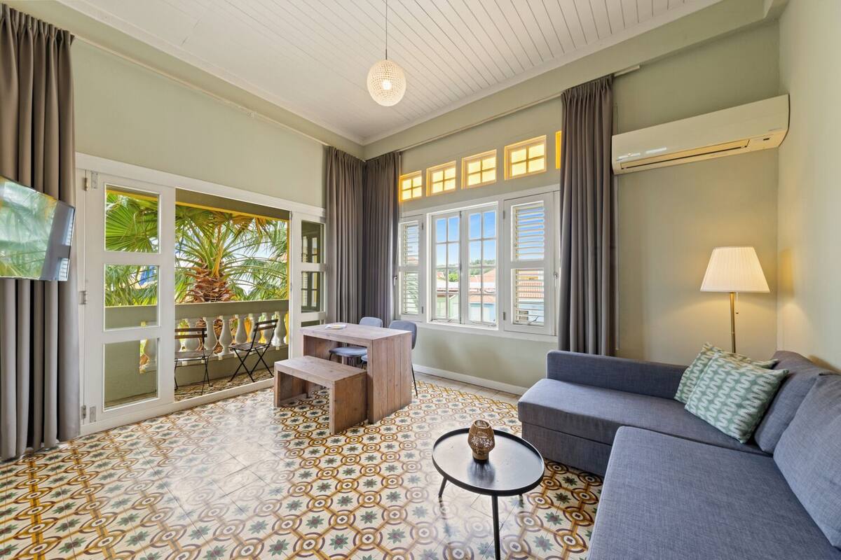 A room with a balcony, a sofa, a table, and a TV.