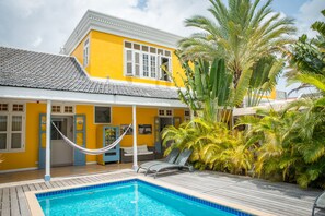 Una casa amarilla con piscina, una hamaca y una tumbona.