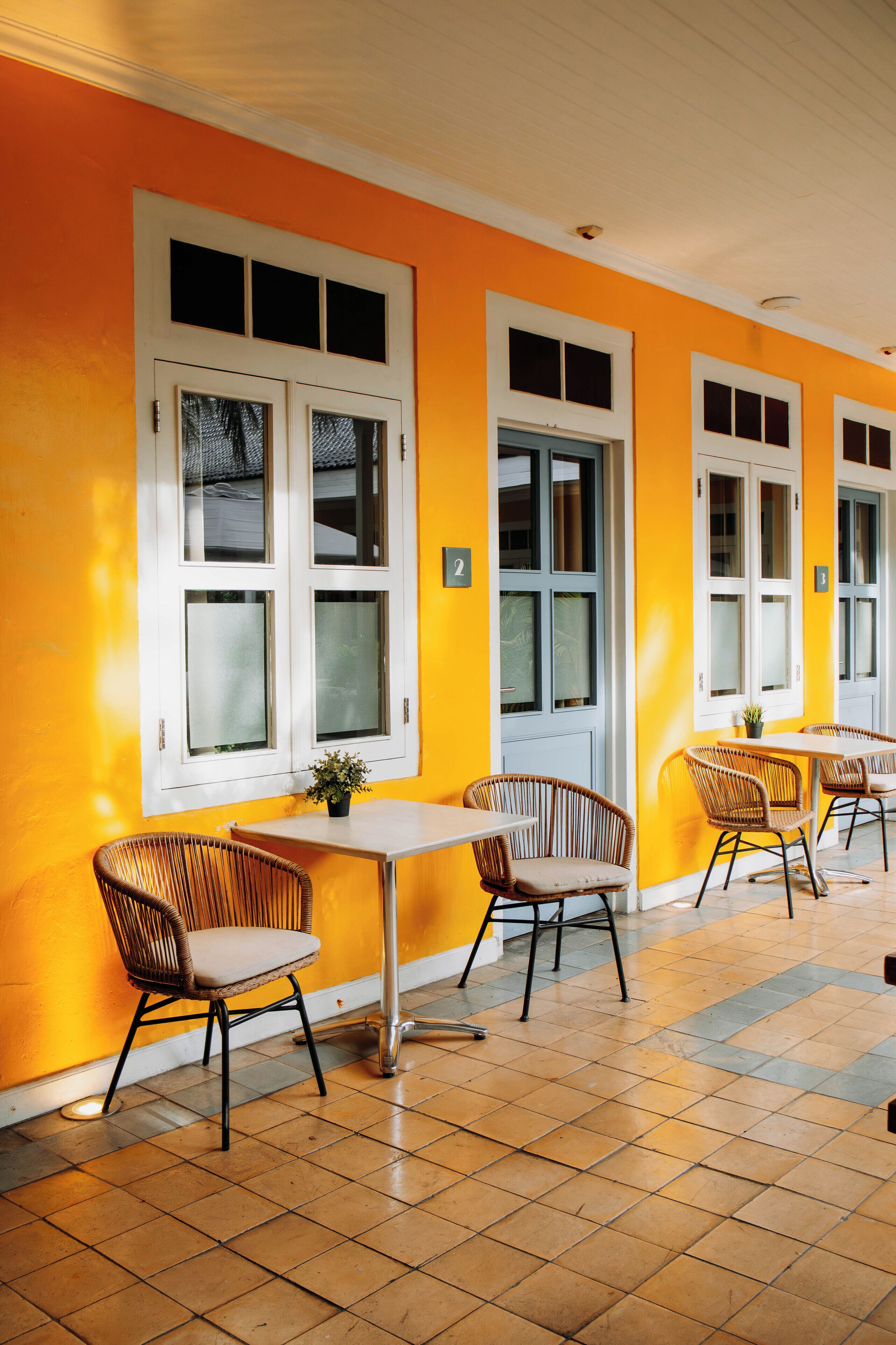 A bright yellow room with white-framed windows, wicker chairs, and a tiled floor.