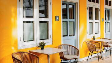 A bright yellow room with white-framed windows, wicker chairs, and a tiled floor.