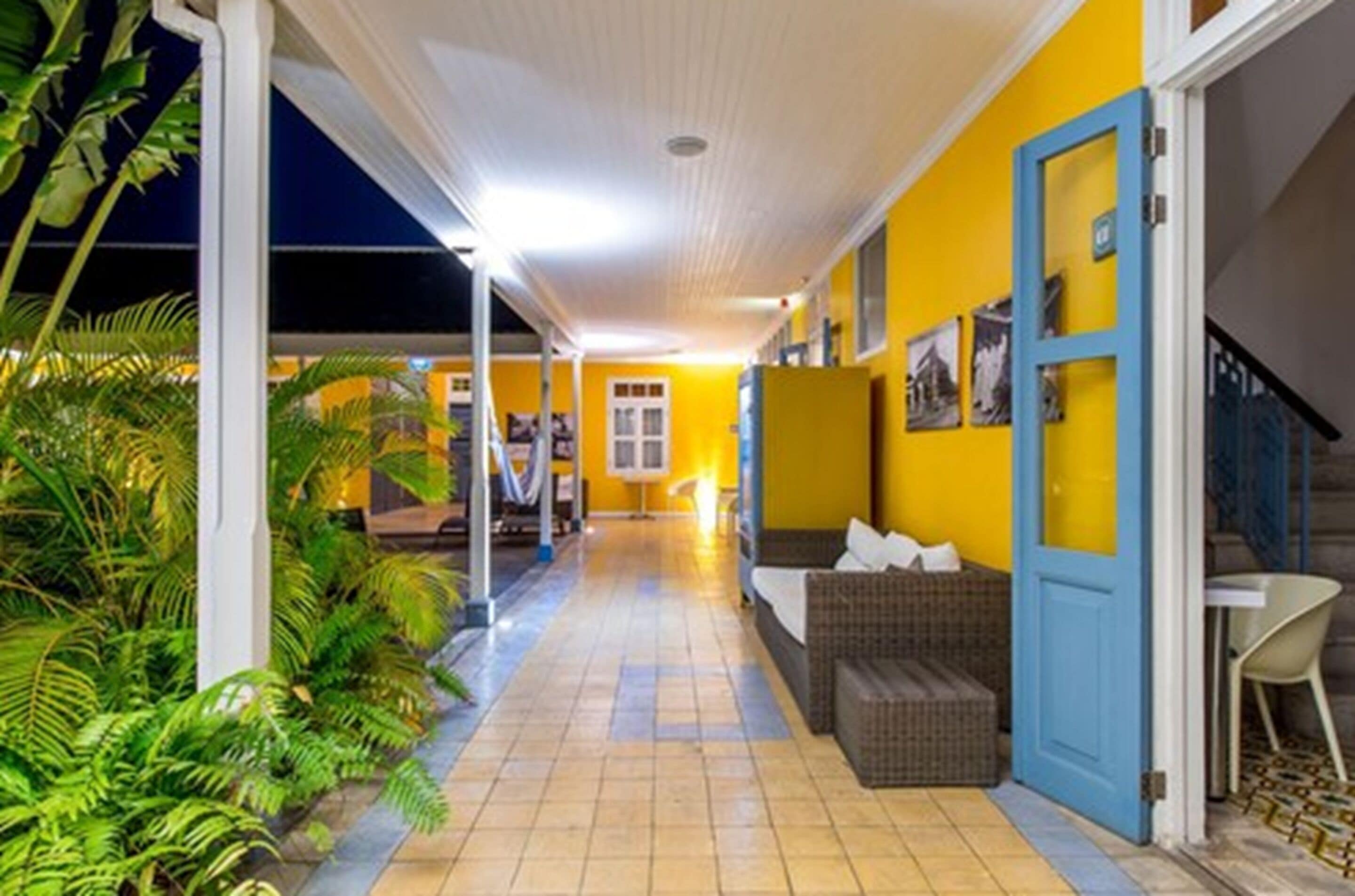 Um corredor com parede amarela, porta azul e sofá de vime.