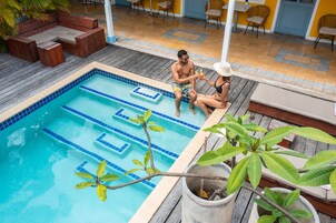 Piscina con azulejos azules y escalones, rodeada de una terraza de madera y sillones de descanso.