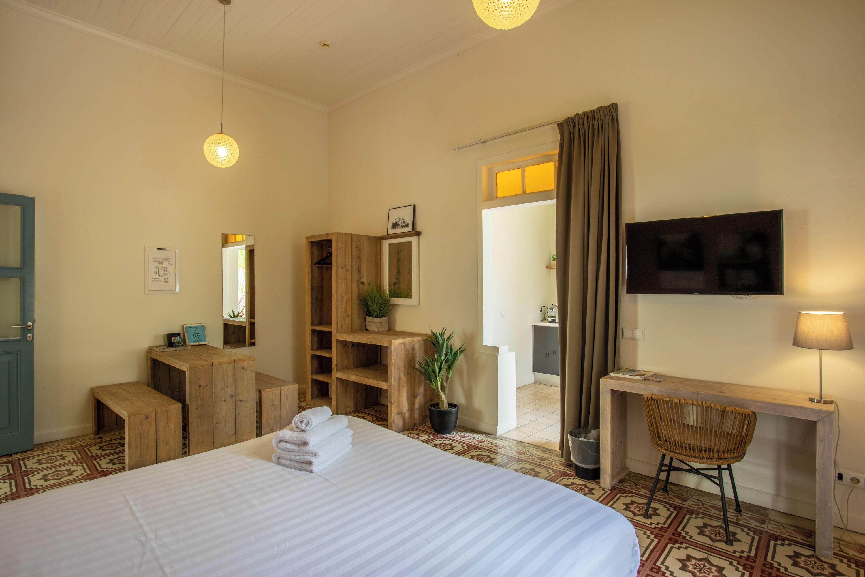Une chambre d’hôtel avec un lit, des meubles en bois, un bureau avec une chaise, une télévision et une plante en pot.