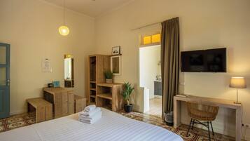 Une chambre d’hôtel avec un lit, des meubles en bois, un bureau avec une chaise, une télévision et une plante en pot.