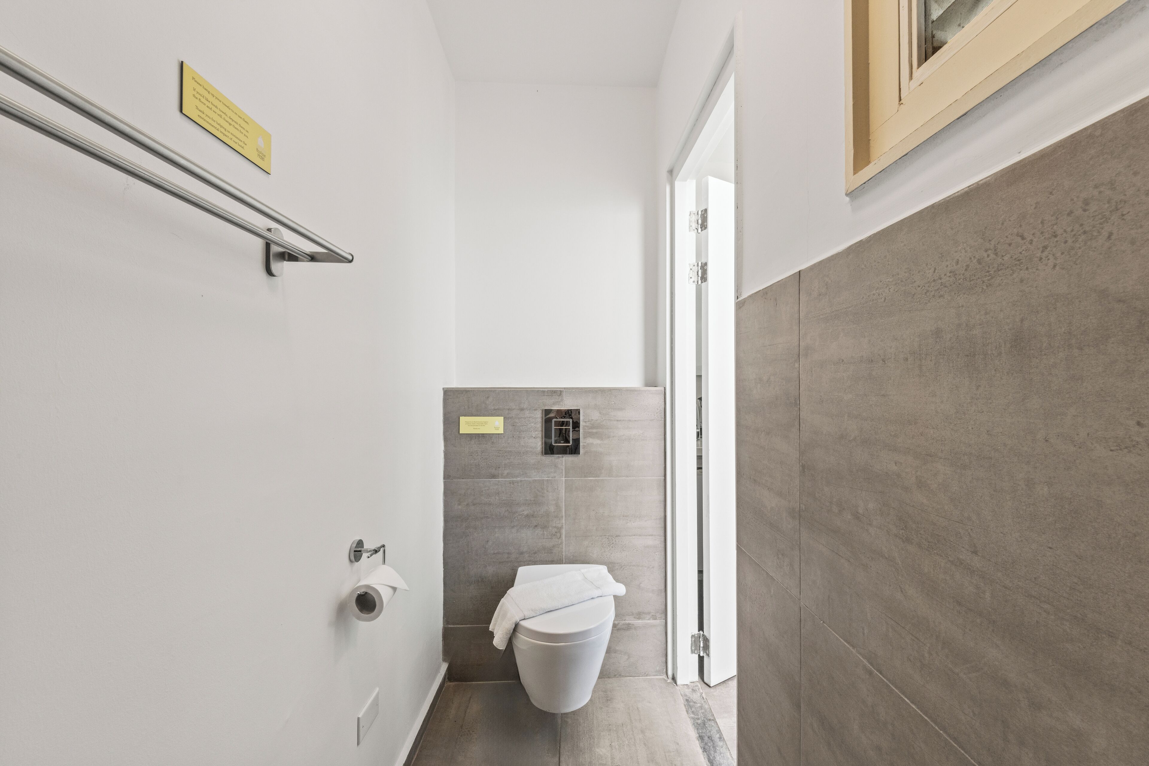 Une petite salle de bain comprenant des toilettes, une barre d’appui et un petit panneau accroché au mur.
