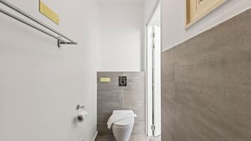 Une petite salle de bain comprenant des toilettes, une barre d’appui et un petit panneau accroché au mur.
