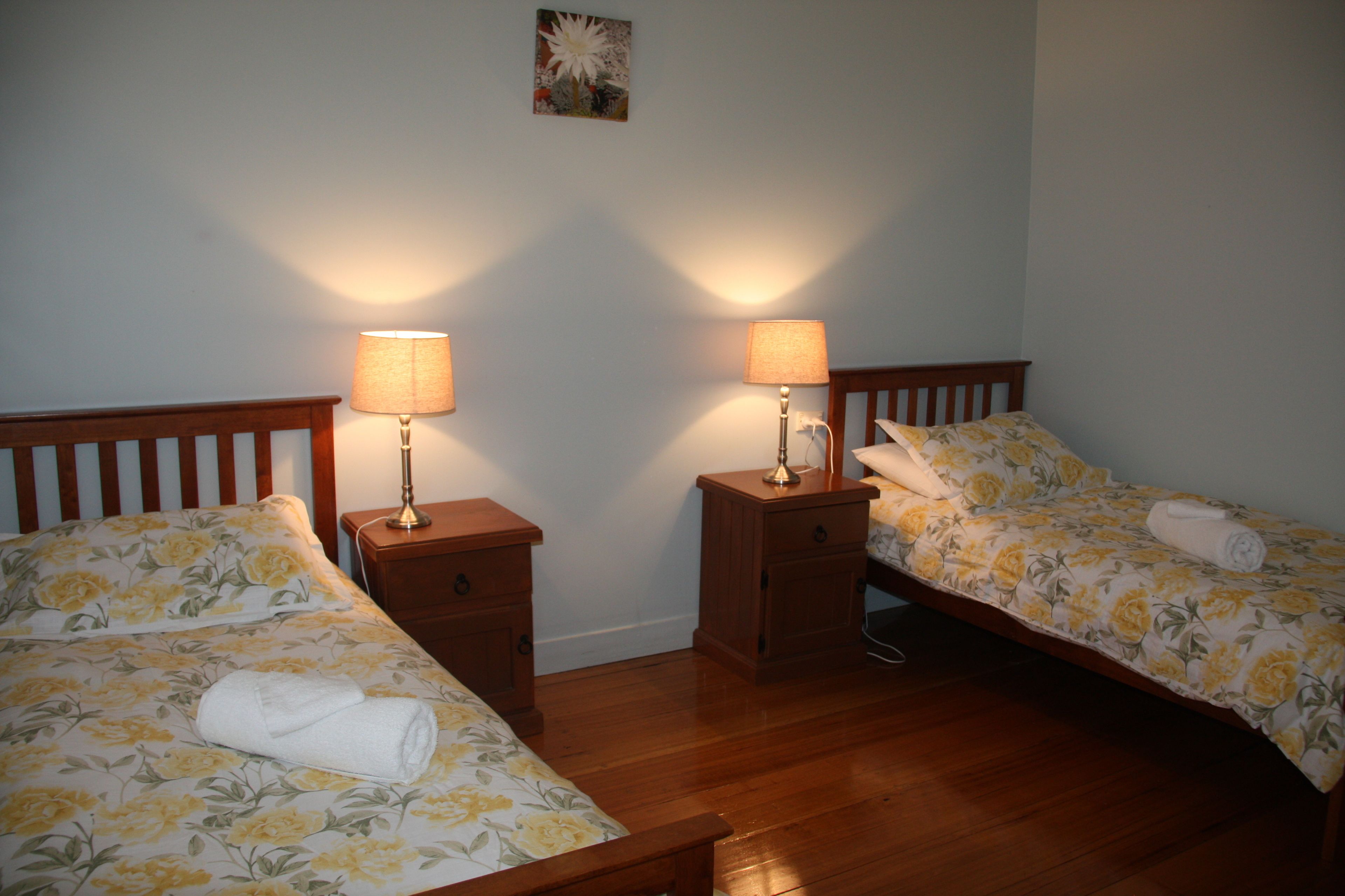 Una camera da letto con due letti singoli, testiere in legno, comodini con lampade e biancheria da letto a motivi floreali.