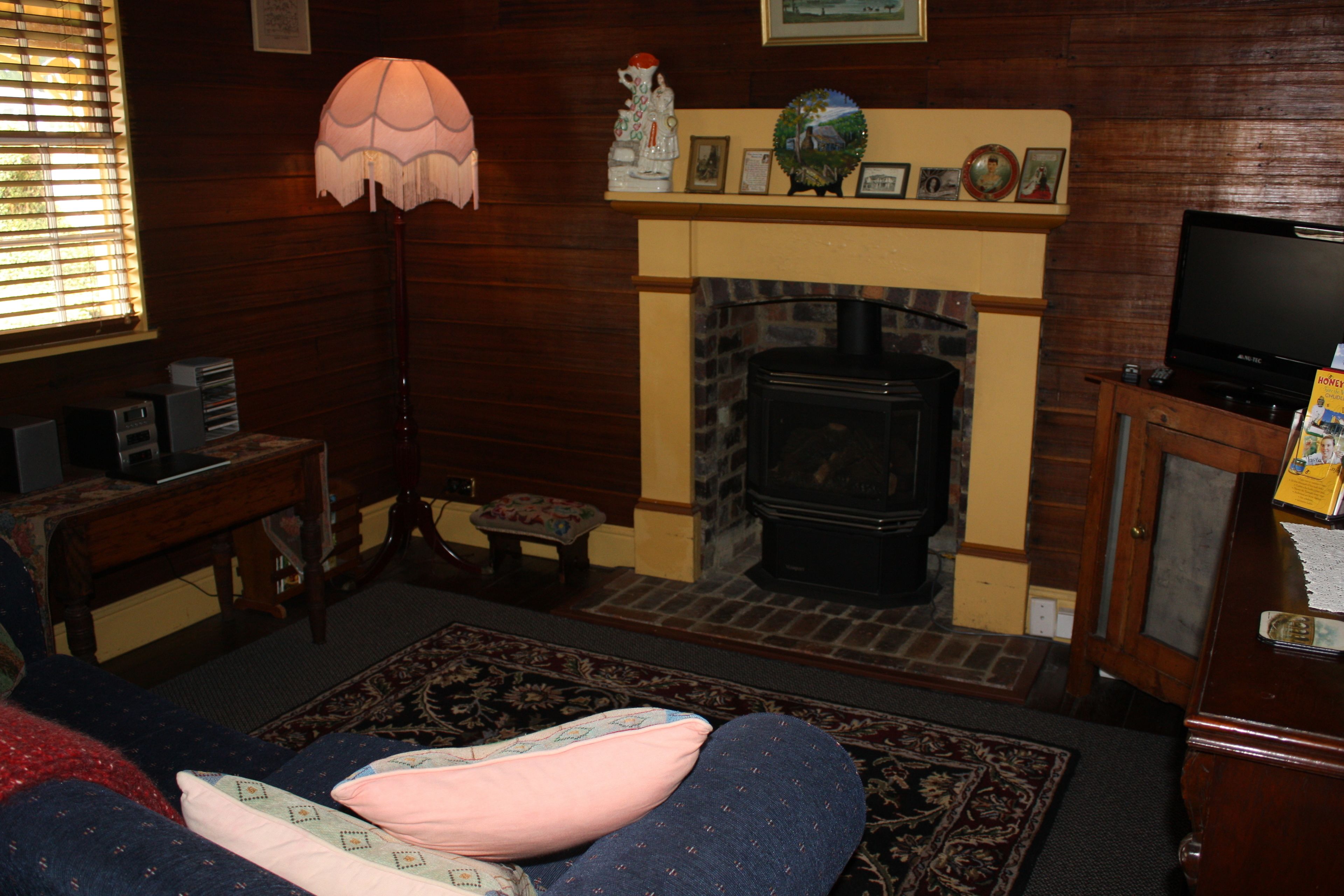A cozy living room with a fireplace, a sofa with a pink cushion, a lamp, and a television on a wooden cabinet.