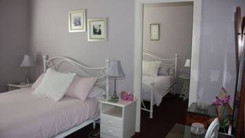 A bedroom with a single bed, bedside tables, a nightstand, a mirror, and framed pictures on the wall.