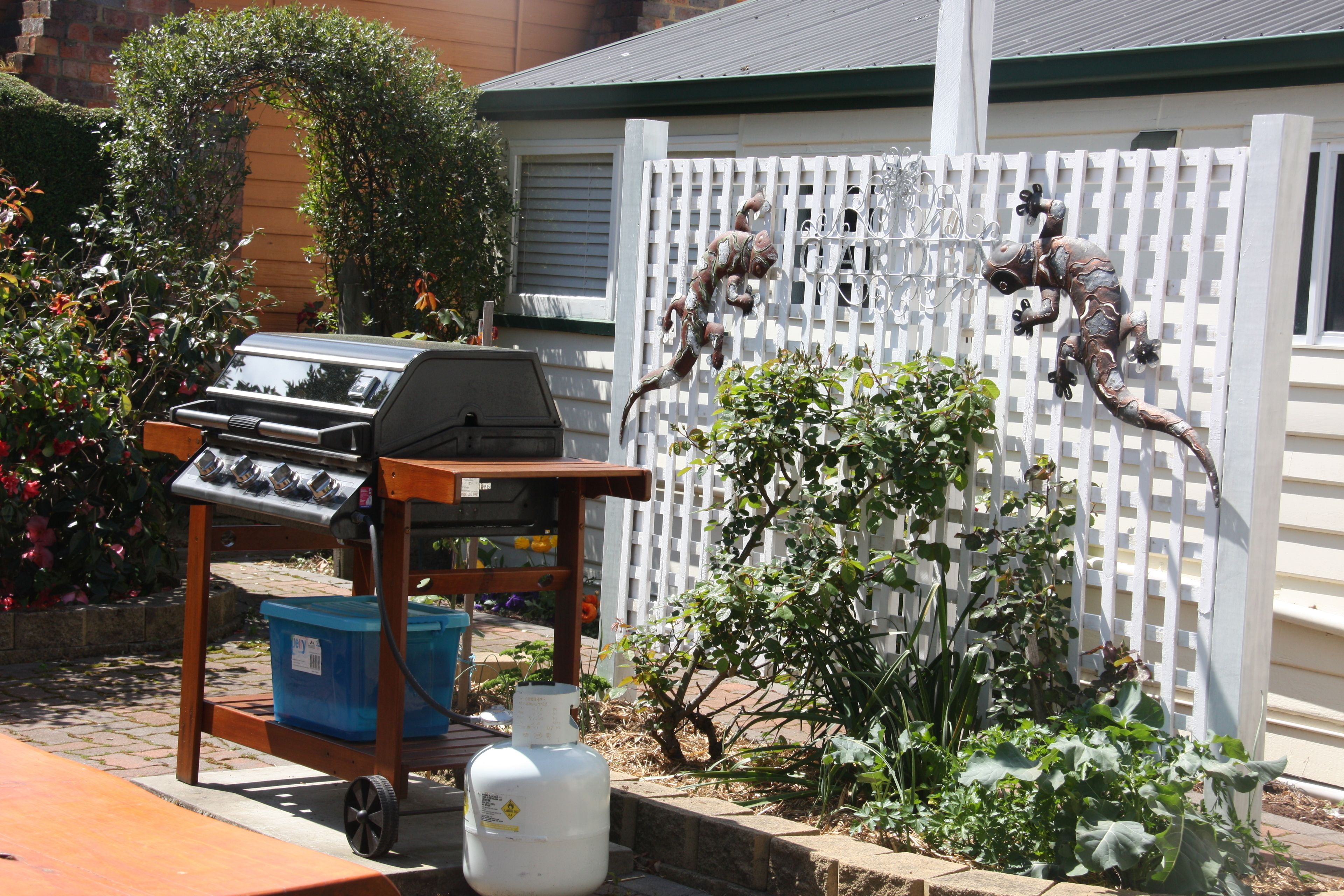 A barbecue grill on a cart, a white picket fence, and a metal sculpture of a lizard.