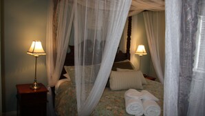 A bedroom with a canopy bed, two bedside lamps, and neatly folded towels on the bed.