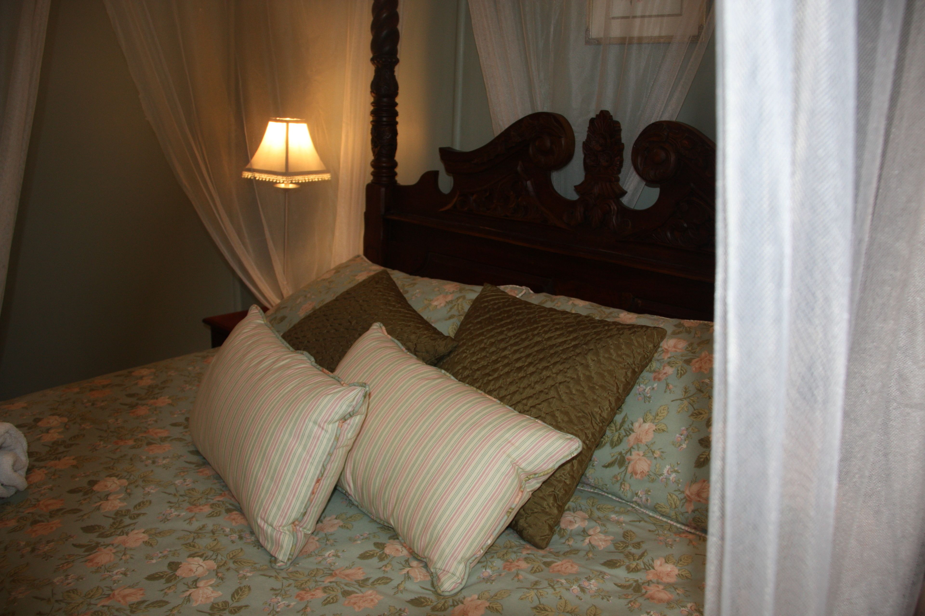 A bed with floral bedding, a canopy, and a bedside lamp.
